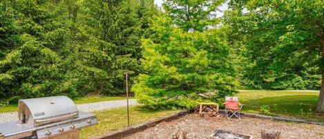 A backyard with a grill, a fire pit, and a chair.