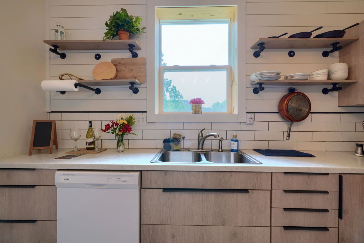 Une cuisine équipée d’un lave-vaisselle encastré, de meubles en bois, d’une fenêtre avec vue et de divers ustensiles de cuisine rangés sur des étagères.