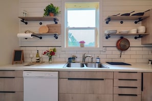 A kitchen with a built-in dishwasher, wooden cabinets, a window with a view, and various kitchen items on shelves.