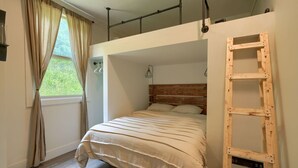 A bedroom with a bunk bed, a wooden ladder, a window with curtains, and a hanging light fixture.