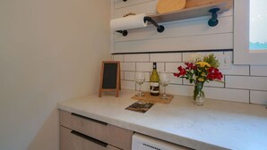 Una cocina con estantes de madera, una pizarra, copas de vino, una botella y un jarrón con flores.