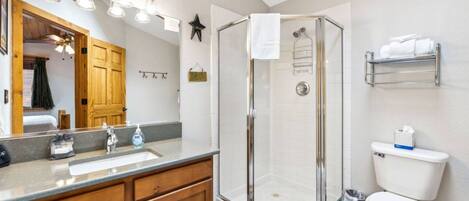 Une salle de bain avec une douche à parois de verre, un lavabo avec un miroir, des meubles en bois et des toilettes.