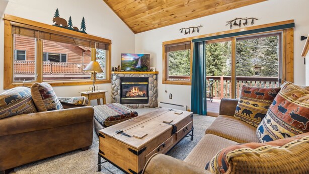 A cozy living room with a fireplace, wooden furniture, and large windows offering a view of the outdoors. - Fall River Hideaway • Peaceful • Near RMNP (Estes Park)
