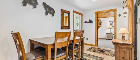 A dining area with a wooden table and chairs, a rug with animal prints, and wall decorations including a mirror and framed pictures.