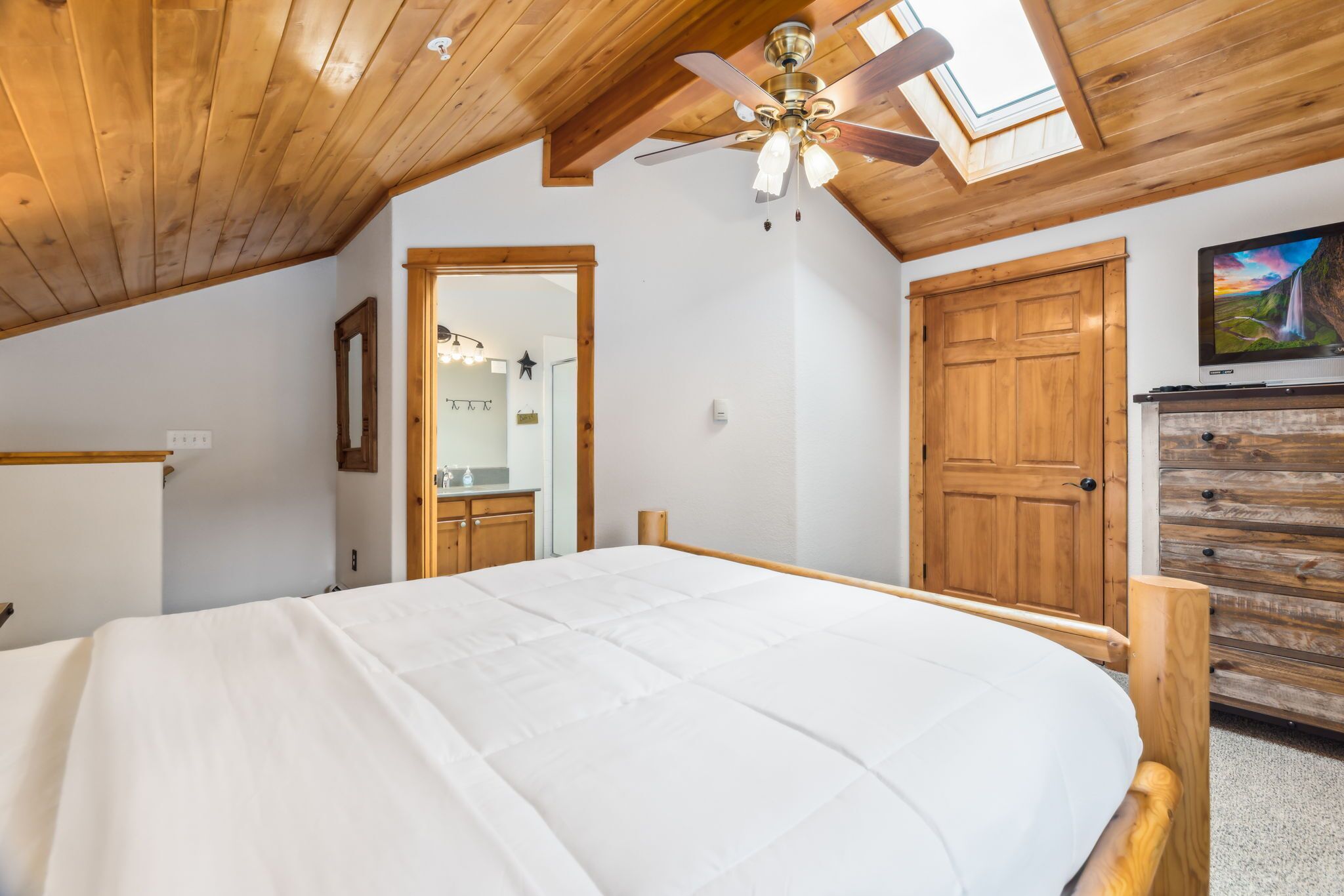 Ein Schlafzimmer mit Bett, Holzboden, Deckenventilator, Fernseher und einer hölzernen Kommode.