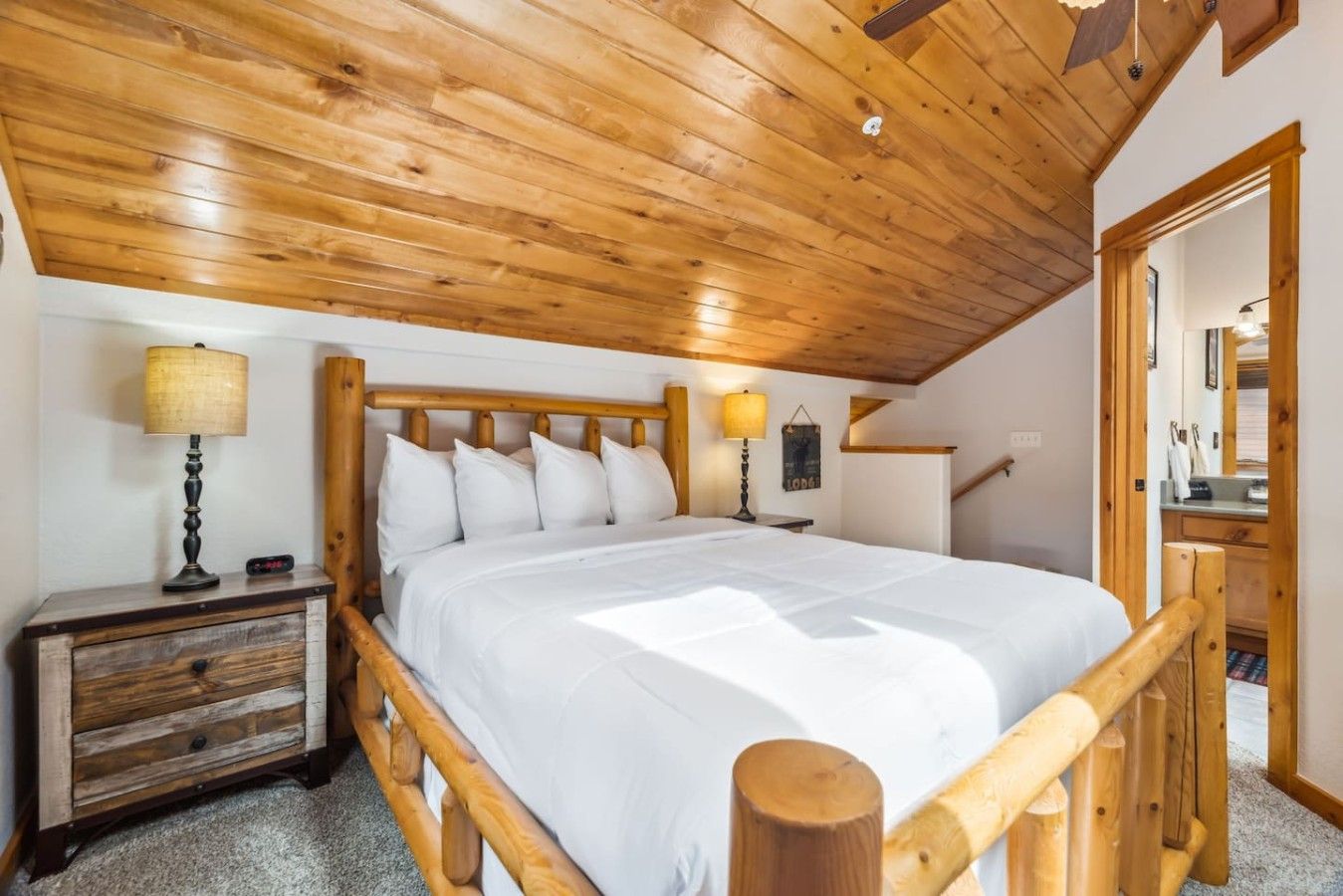 A bedroom with a wooden bed frame, white bedding, a nightstand with a lamp, and a wooden headboard.