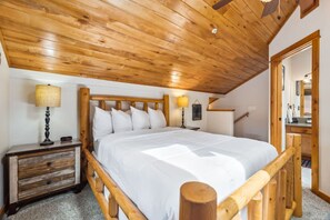 Een slaapkamer met een houten bedframe, wit beddengoed, een nachtkastje met een lamp en een houten hoofdeinde.