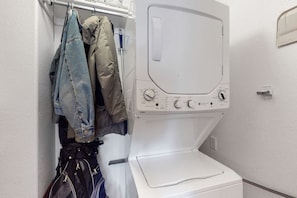 A laundry area with a washing machine and dryer, a clothes rack with hanging garments, and a small storage cabinet.