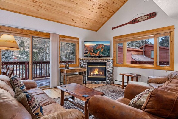 A cozy living room with a fireplace, leather sofas, and large windows offering views of a snowy landscape.