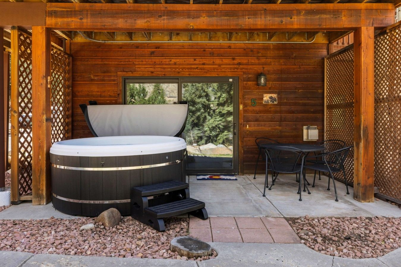 A hot tub with a bench, a table, and chairs in a wooden outdoor area.