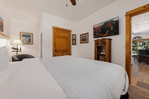 A bedroom with a bed, a desk, a chair, a wooden door, a bookshelf, and a painting on the wall.