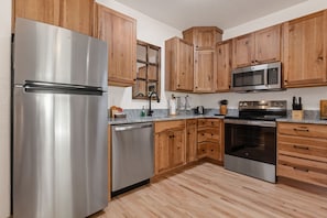 A kitchen with wooden cabinets, stainless steel appliances, and a granite countertop. - Riverfront Hideaway • Private Hot Tub (Estes Park)