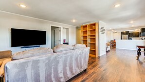 A living room with a large flat-screen TV, a beige sofa, wooden shelves, and a kitchen area with a refrigerator and cabinets. - Flagstaff Home w/ Grill: 3 Mi to Historic Downtown (Flagstaff)