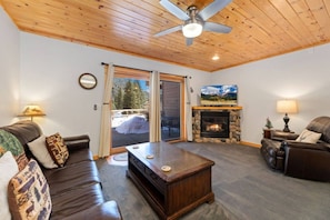 A cozy living room with a fireplace, leather sofas, a coffee table, and a ceiling fan.