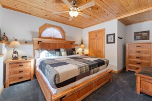 A bedroom with a wooden bed, two bedside tables, a nightstand, a ceiling fan, and a wooden wardrobe.