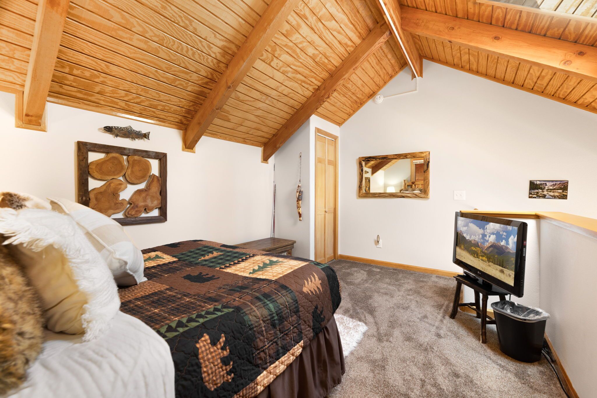 Un dormitorio con techo de madera, una cama con colcha, un televisor y un espejo en la pared.