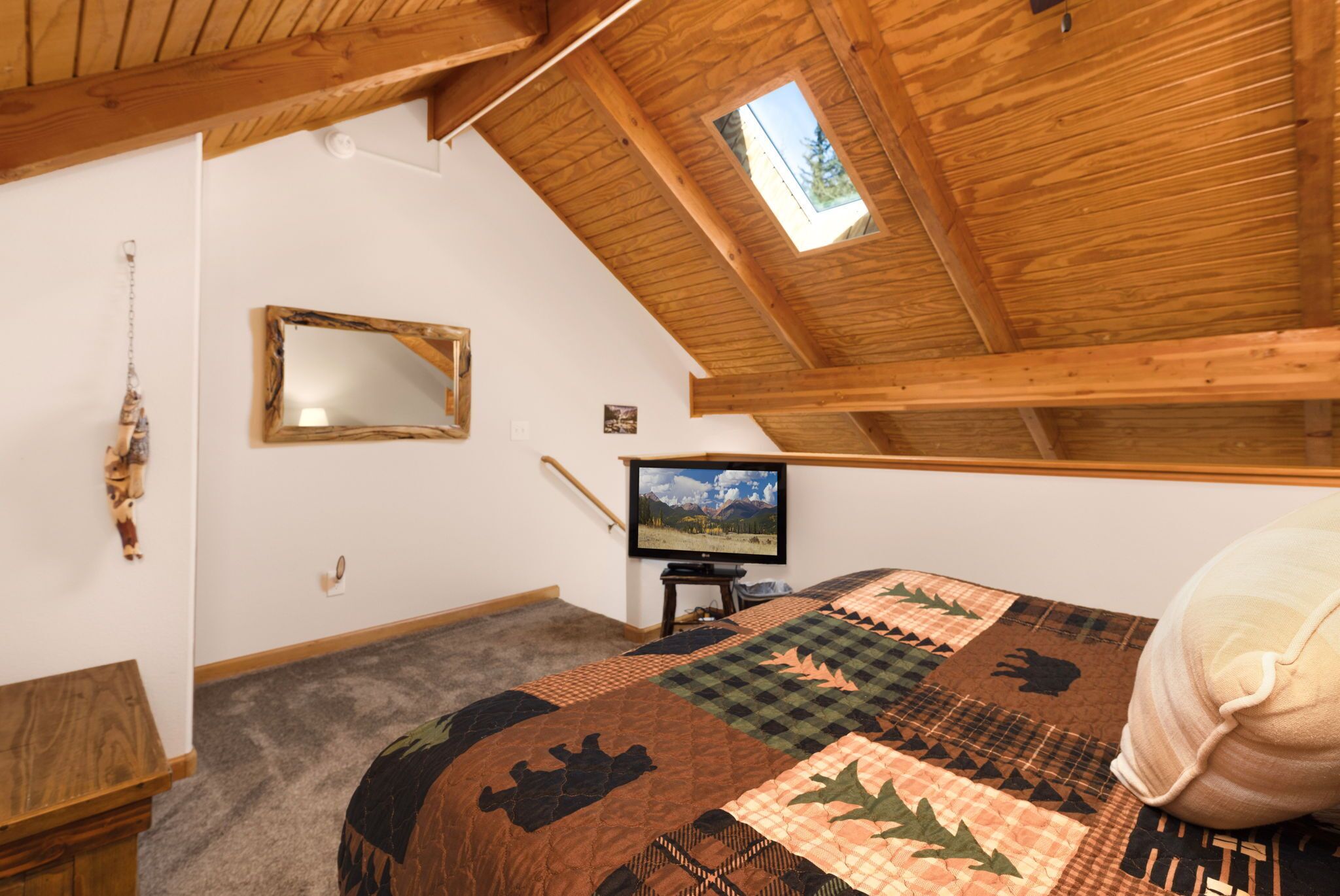A bedroom with a sloped ceiling, a wooden bed frame, a quilt, a television, and a small window.