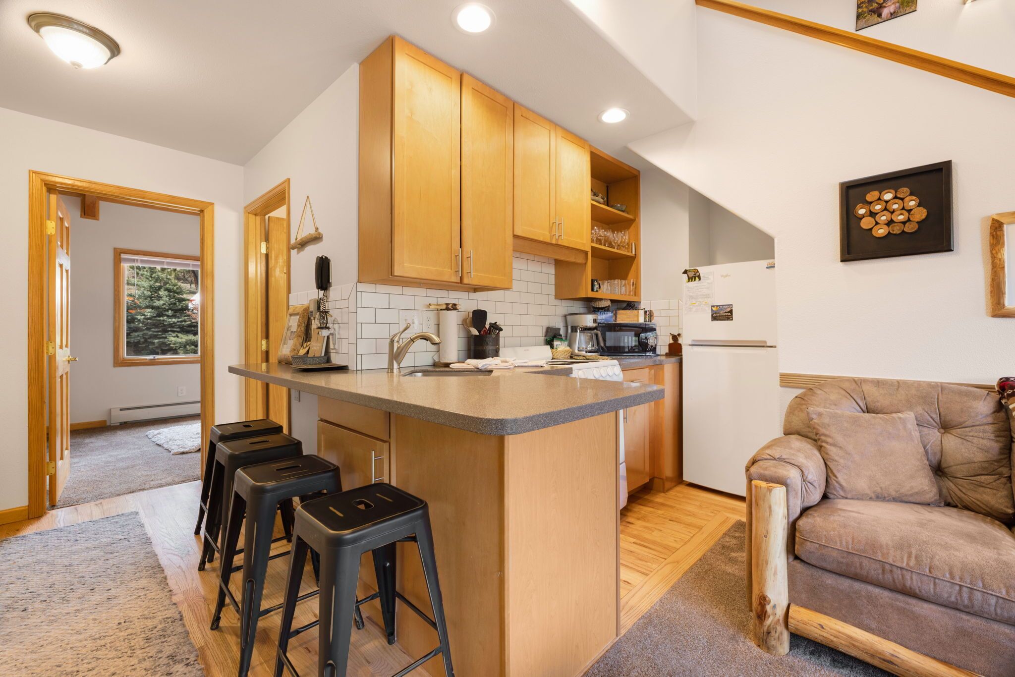A modern kitchen with wooden cabinets, a central island with stools, and a refrigerator.