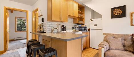 A modern kitchen with wooden cabinets, a central island with stools, and a refrigerator.