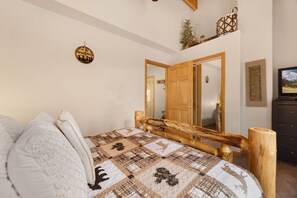A bedroom with a wooden bed frame, a quilt, a mirror, and a television. - Scenic Riverfront Escape • RMNP • River Views (Estes Park)