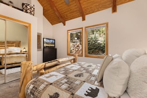 A bedroom with a wooden bed, a television, and a window with a view of trees. - Scenic Riverfront Escape • RMNP • River Views (Estes Park)