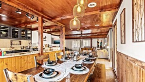 Un comedor amplio con una larga mesa de madera dispuesta para una comida, vigas de madera en el techo y una decoración rústica.