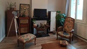 Un saló amb una taula de centre de fusta, dos seients còmodes, un trípode, una televisió i una llar de foc.