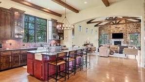 A spacious kitchen with a large island, bar stools, and a stone fireplace. - Luxe Tuscan Villa on 1 Acre with Pool & Pickleball, Sleeps 18, 9 mins to DT (Sunset Valley)