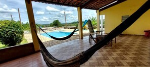 A hammock in a covered outdoor area with a pool and a view of the landscape. - Chácara Roteiro do Vinho com Wi-fi (Canguera)
