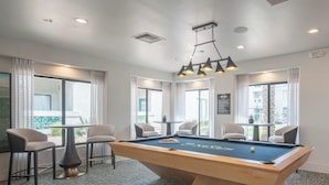 A pool table with chairs, a ceiling light fixture, and large windows with curtains.