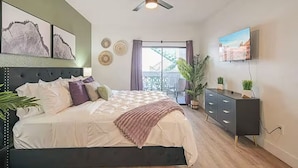 A bedroom with a bed, a ceiling fan, a TV, and a balcony with a view.