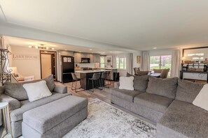 A modern living room with a grey sectional sofa, a kitchen with grey cabinets, and a dining area with a bar.