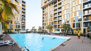 A swimming pool surrounded by a wooden deck with lounge chairs and palm trees.