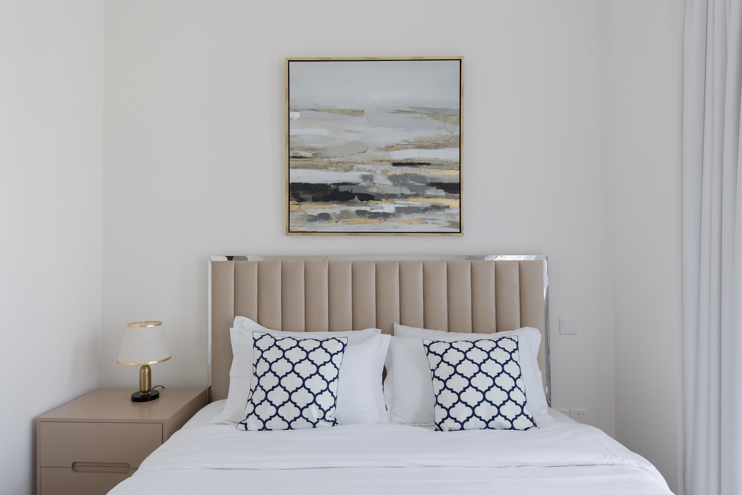 A neatly arranged hotel room with a bed, a bedside lamp, and a framed abstract painting on the wall.