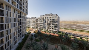 A modern multi-story building with balconies, a landscaped courtyard with palm trees, and a view of a river.