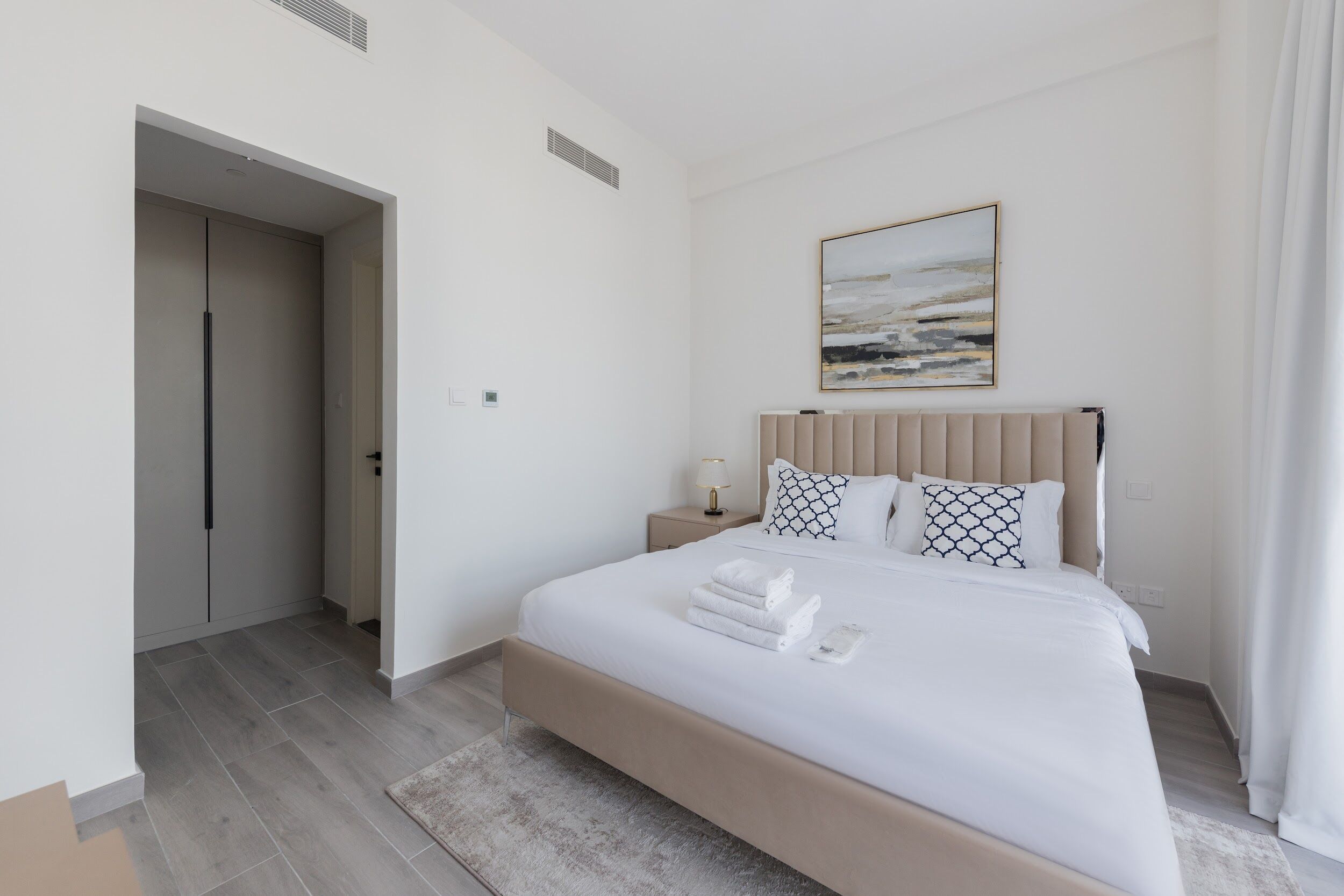A modern bedroom with a large bed, a bedside table with a lamp, and a painting on the wall.