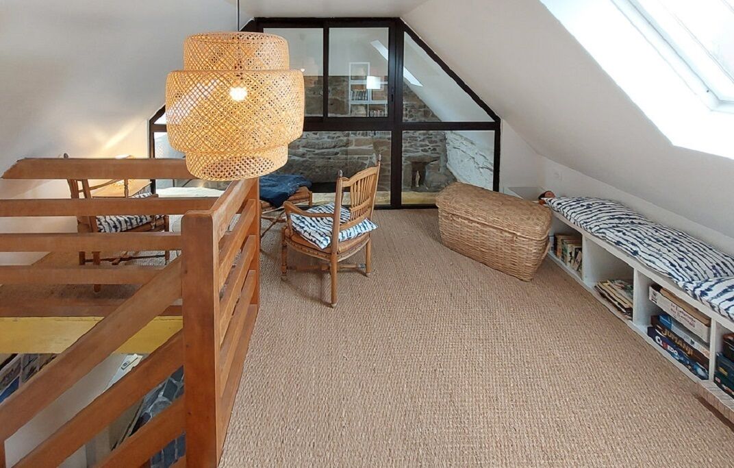 Een slaapkamer met een vide, schuine wanden, een houten bed, een rieten stoel, een boekenkast en een groot raam.