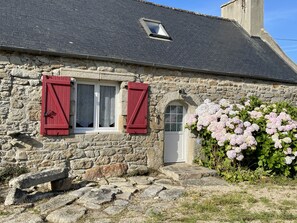 A stone building with red shutters, a white door, and a small window. - Fermette Bretonne Typique en Pierres au Bout du Bout du Finistère Pays des Abers (Plouguerneau)