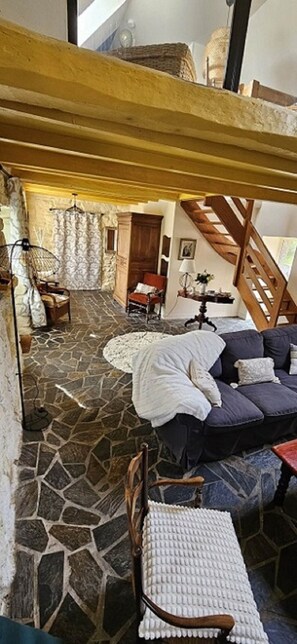 A cozy interior with a stone floor, a wooden staircase, a sofa, and a chair. - Fermette Bretonne Typique en Pierres au Bout du Bout du Finistère Pays des Abers (Plouguerneau)