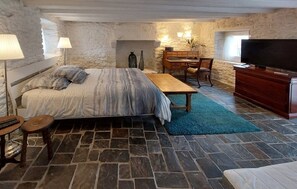 A bedroom with a stone wall, a bed, a desk, a chair, a TV, and a blue rug. - Fermette Bretonne Typique en Pierres au Bout du Bout du Finistère Pays des Abers (Plouguerneau)