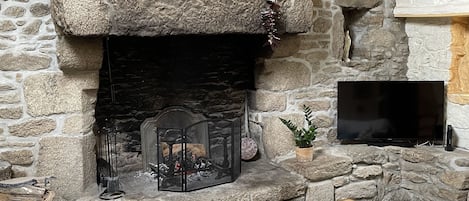 A stone fireplace with a television mounted above it, a wooden table, a cushioned chair, and a sofa with a throw pillow.