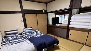 A traditional Japanese-style room with tatami flooring, a bed with striped bedding, a television, and a wardrobe with folded clothes. - Entire old house rental, complete rental, private sauna (Saga)