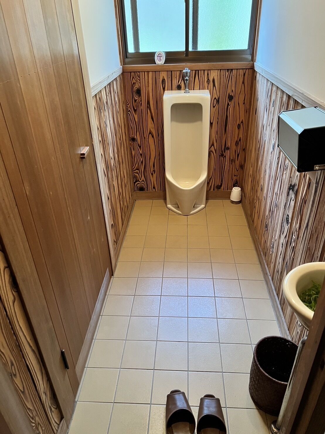 Et lille, aflangt badeværelse med et træskab, en pissoir og et toilet.