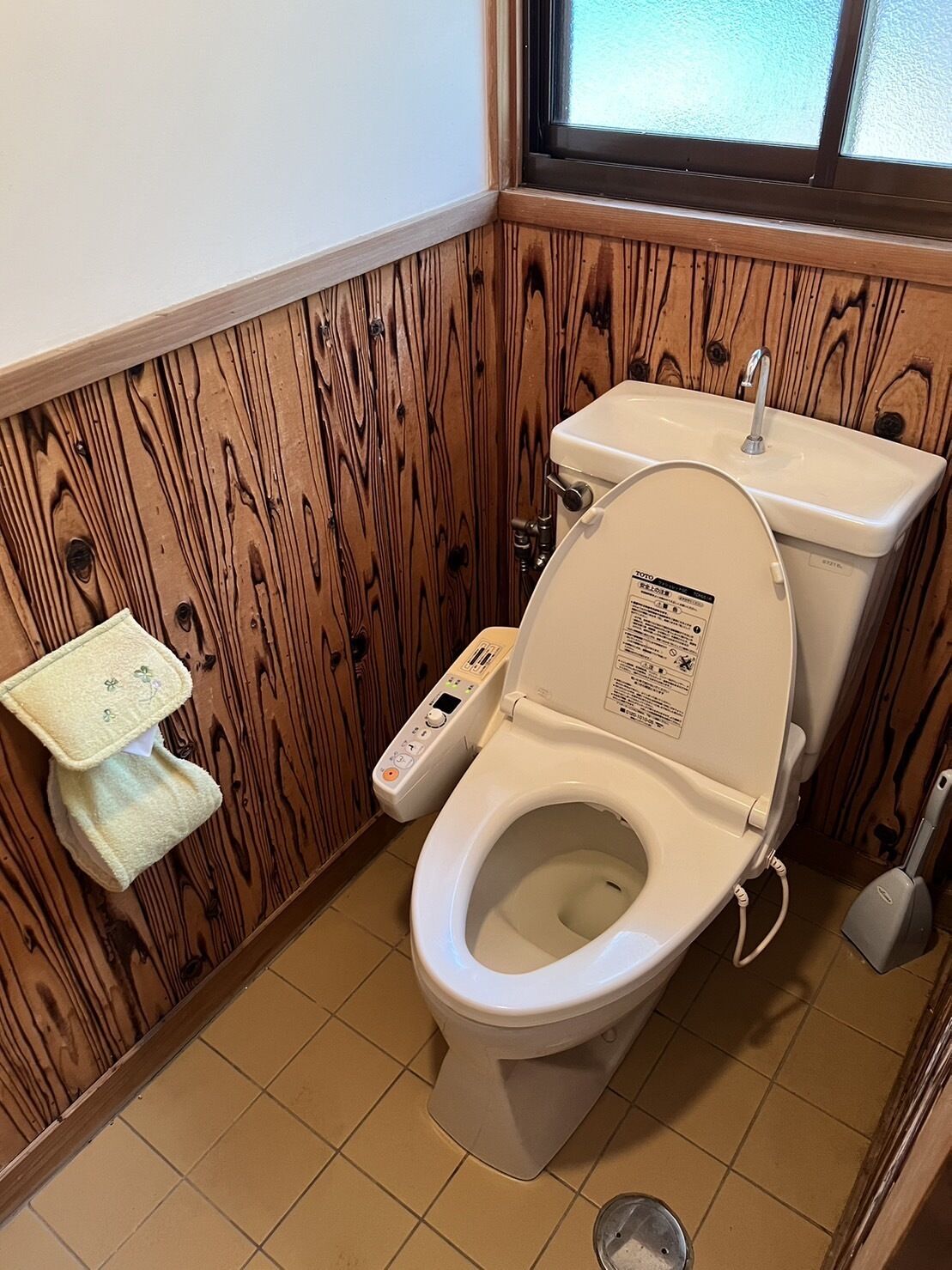 A bathroom with a wooden panel wall, a white toilet with a control panel, a small sink, and a window above the toilet.