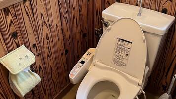 A bathroom with a wooden panel wall, a white toilet with a control panel, a small sink, and a window above the toilet.