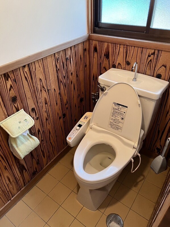A bathroom with a wooden panel wall, a white toilet with a control panel, a small sink, and a window above the toilet.