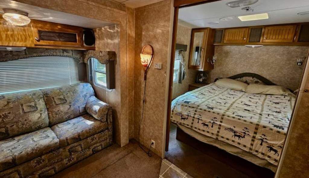 An RV interior with a sofa, a bed with patterned bedding, and wooden cabinets.