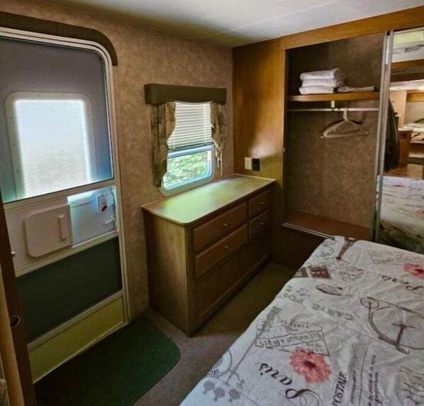 Een kleine slaapkamer met een bed, een dressoir en een raam met zonwering.
