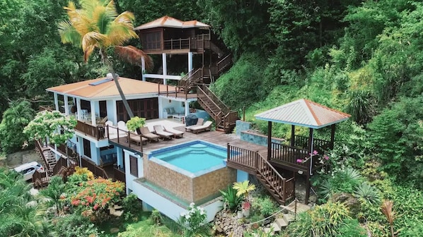 Et hus med flere etager og swimmingpool, omgivet af frodig vegetation.