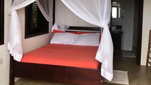 Ein Bett mit roter Matratze und weißer Bettwäsche, ein Deckenventilator und ein Fenster mit Jalousien.